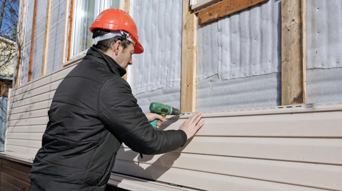 Siding replacement professional using a power drill to install new tan vinyl siding on a home exterior in Sarasota, FL
